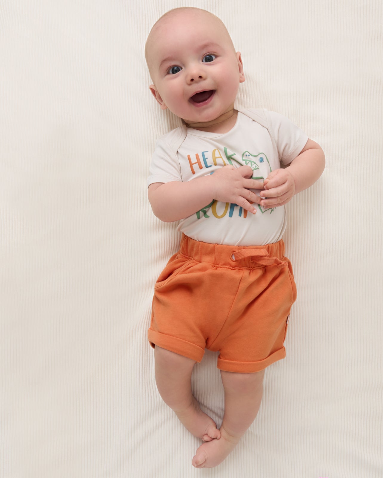 Baby wearing the Orange Haze Cuffed Baby Shorts with a dino bodysuit