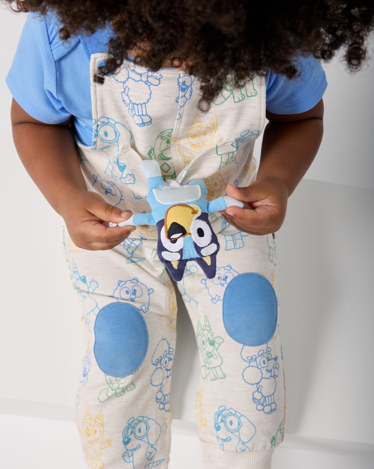 Child holding the plushie in the pocket of the Bluey Playtime Crew Overall