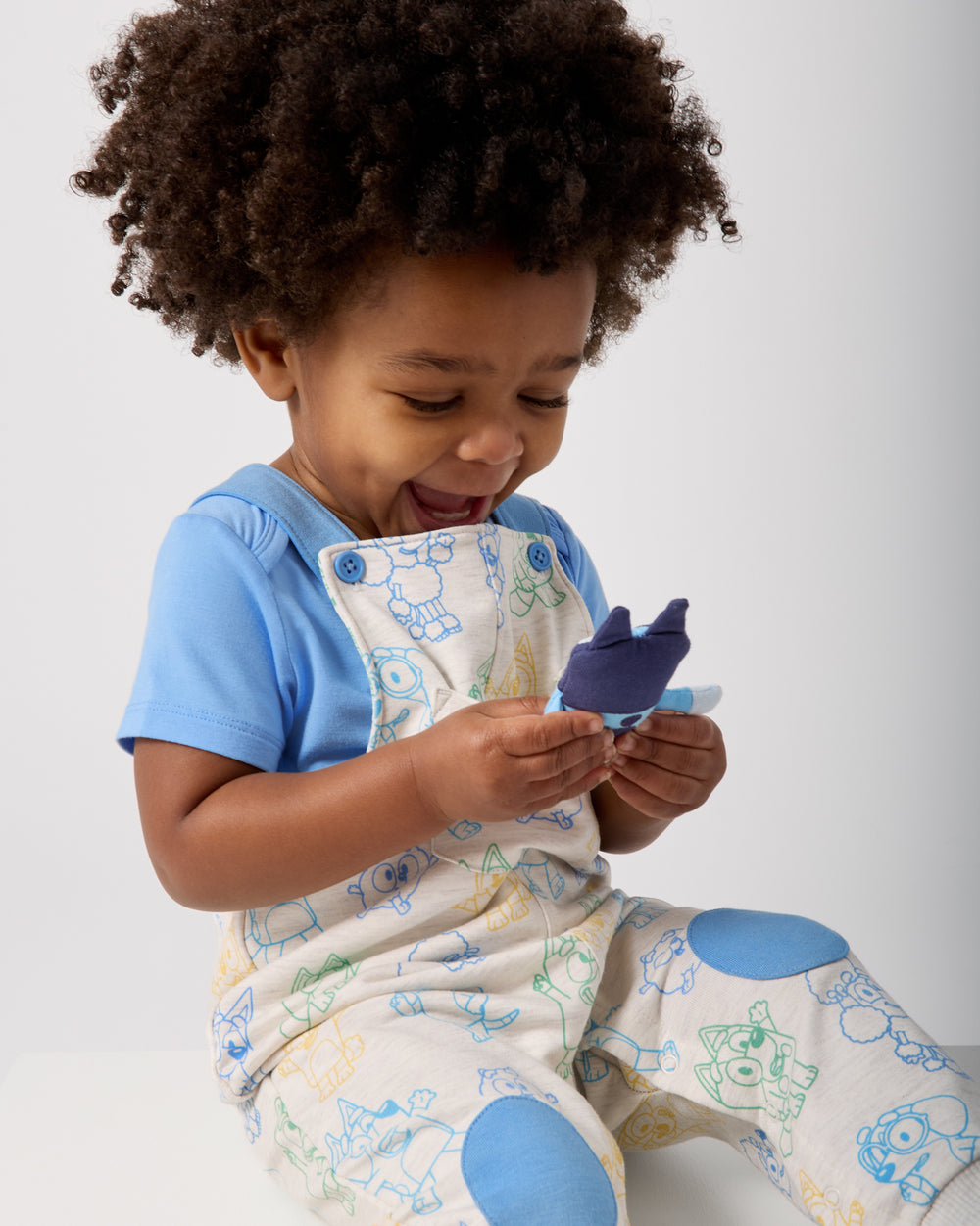 Child holding the Bluey plush toy in the Bluey Playtime Crew Overall pocket