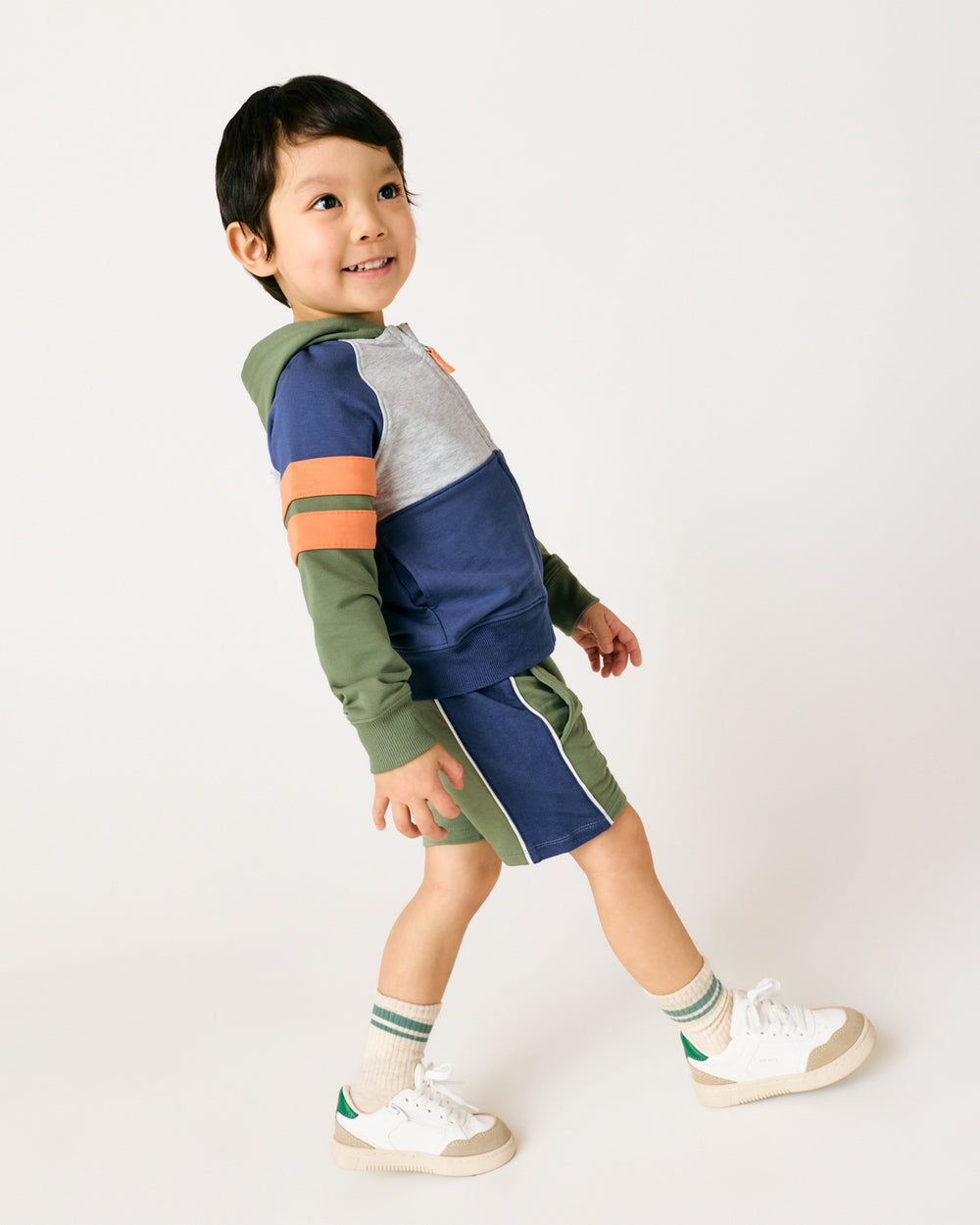 Walking boy wearing the Moss Piped Short with a matching hoodie