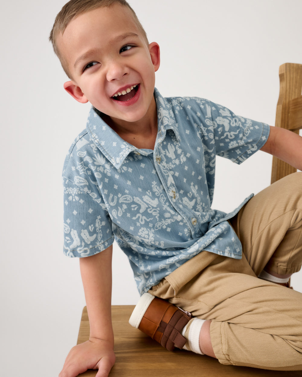 Boy on a wooden chair wearing the Bandana Blues Denim Button Down Polo