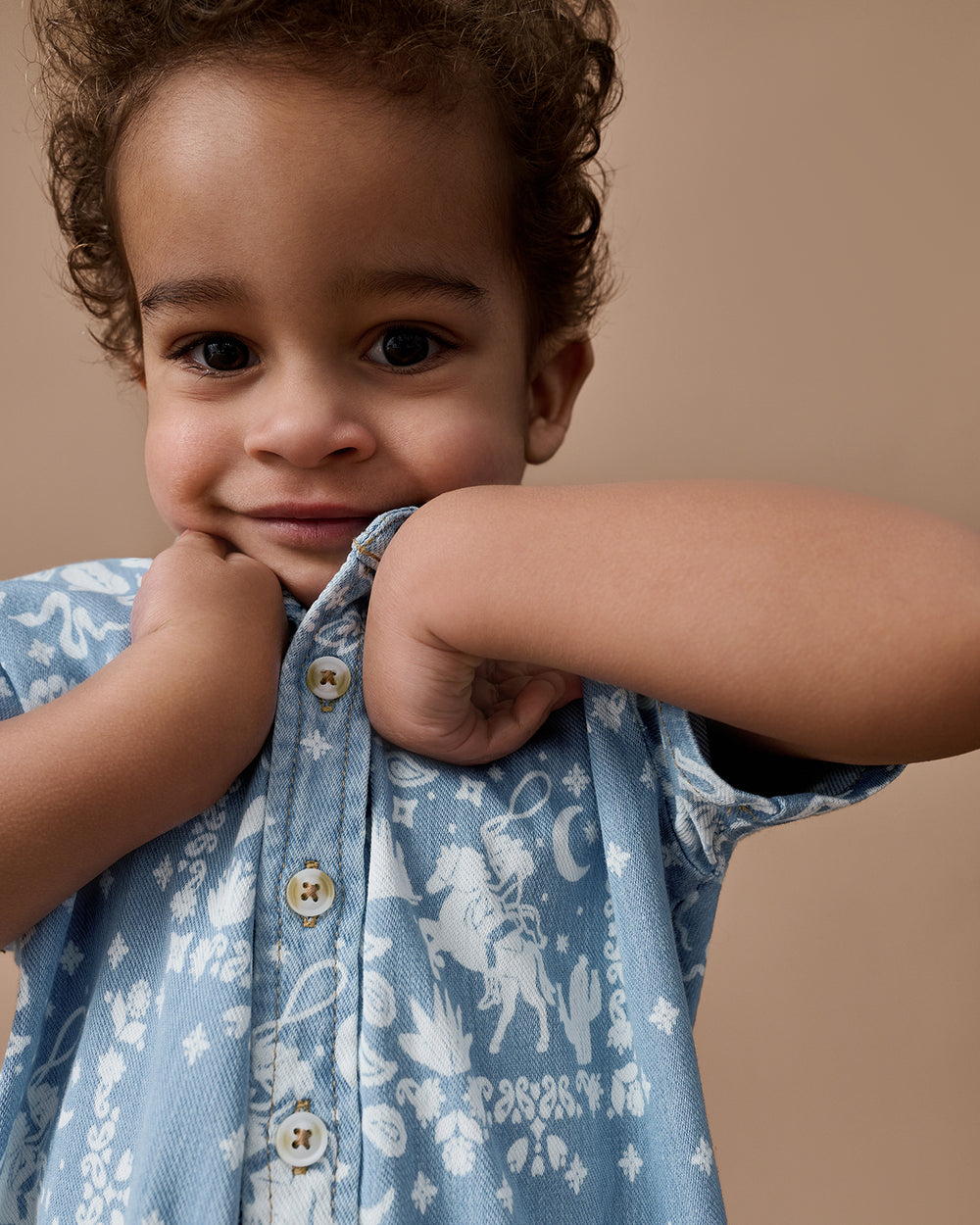 Close up of boy wearing the Bandana Blues Denim Button Down Polo on a brown background