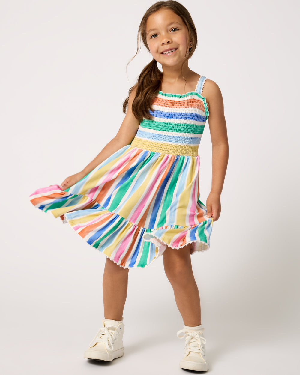 Girl wearing the Rainbow Ribbon Smocked Tank Dress with white sneakers