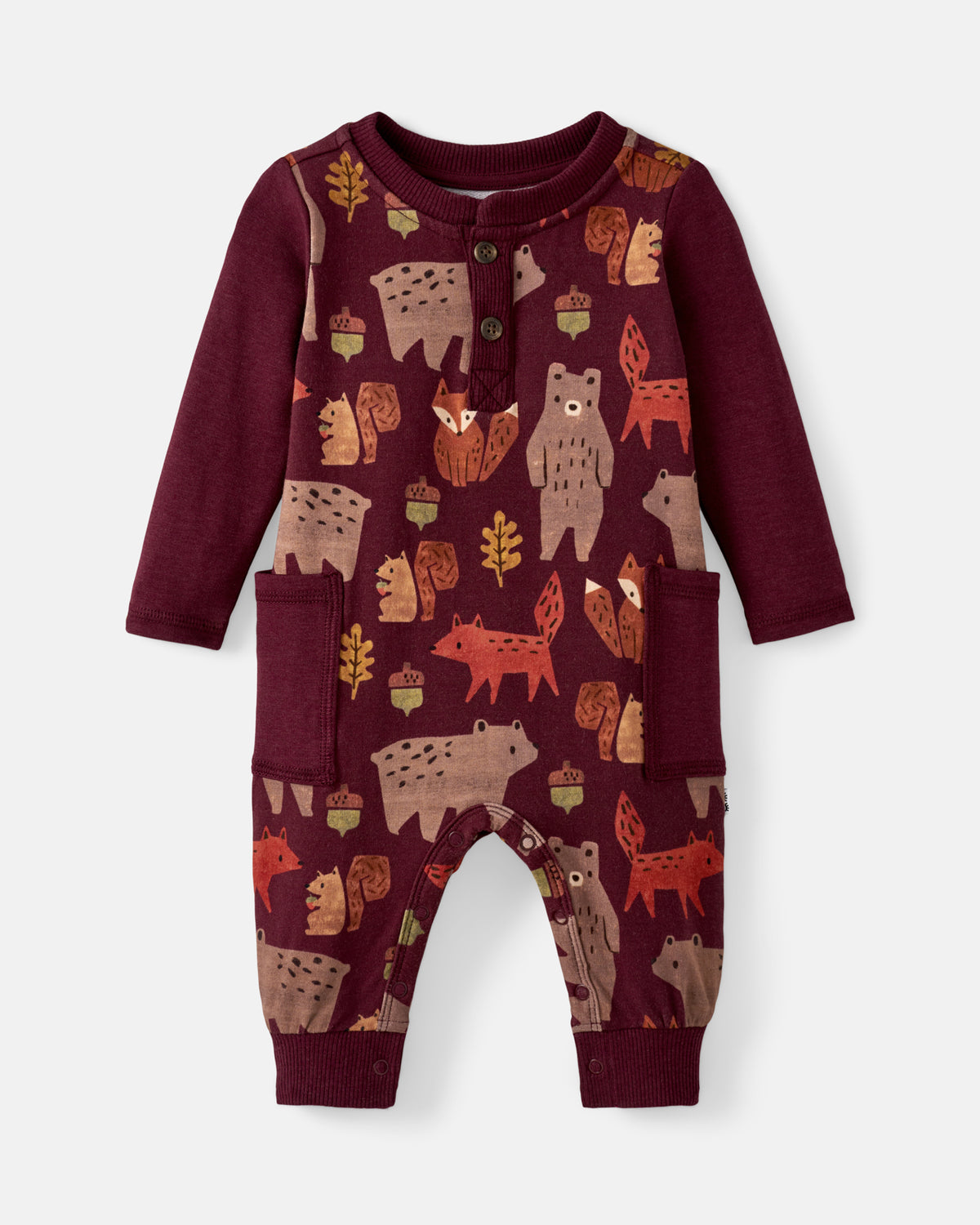A baby long-sleeve romper in deep burgundy with an all-over woodland forest print of bears, foxes, acorns, and leaves, featuring a buttoned henley neckline and front pockets.