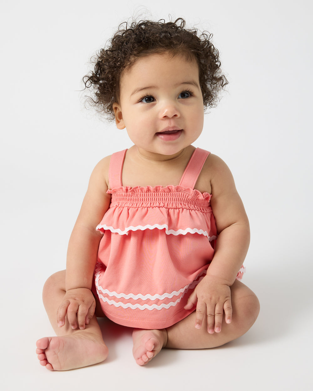Sitting baby wearing the Beach Coral Smocked Top with Bloomer