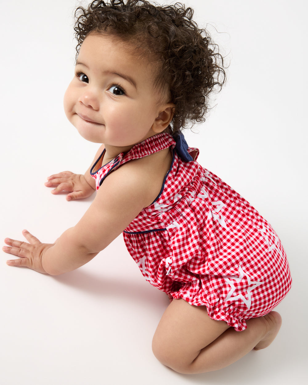 Crawling baby wearing the Celebration Gingham Bow Back Bubble Romper