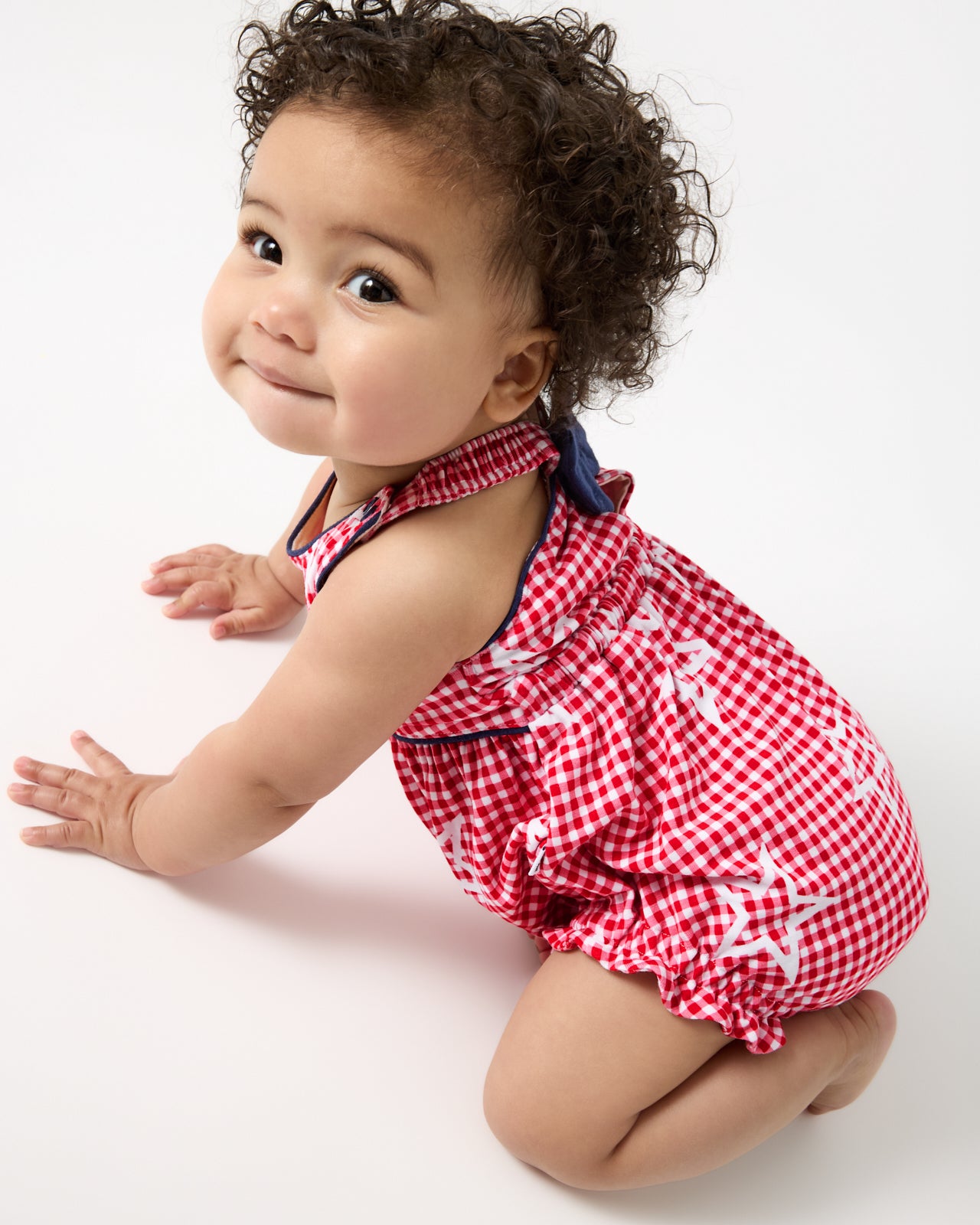 Crawling baby wearing the Celebration Gingham Bow Back Bubble Romper
