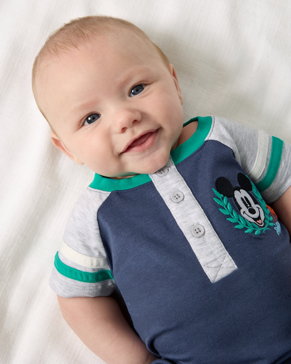 Close up aerial view of baby wearing the Disney Mickey Mouse Sports Club Henley Shorty Romper