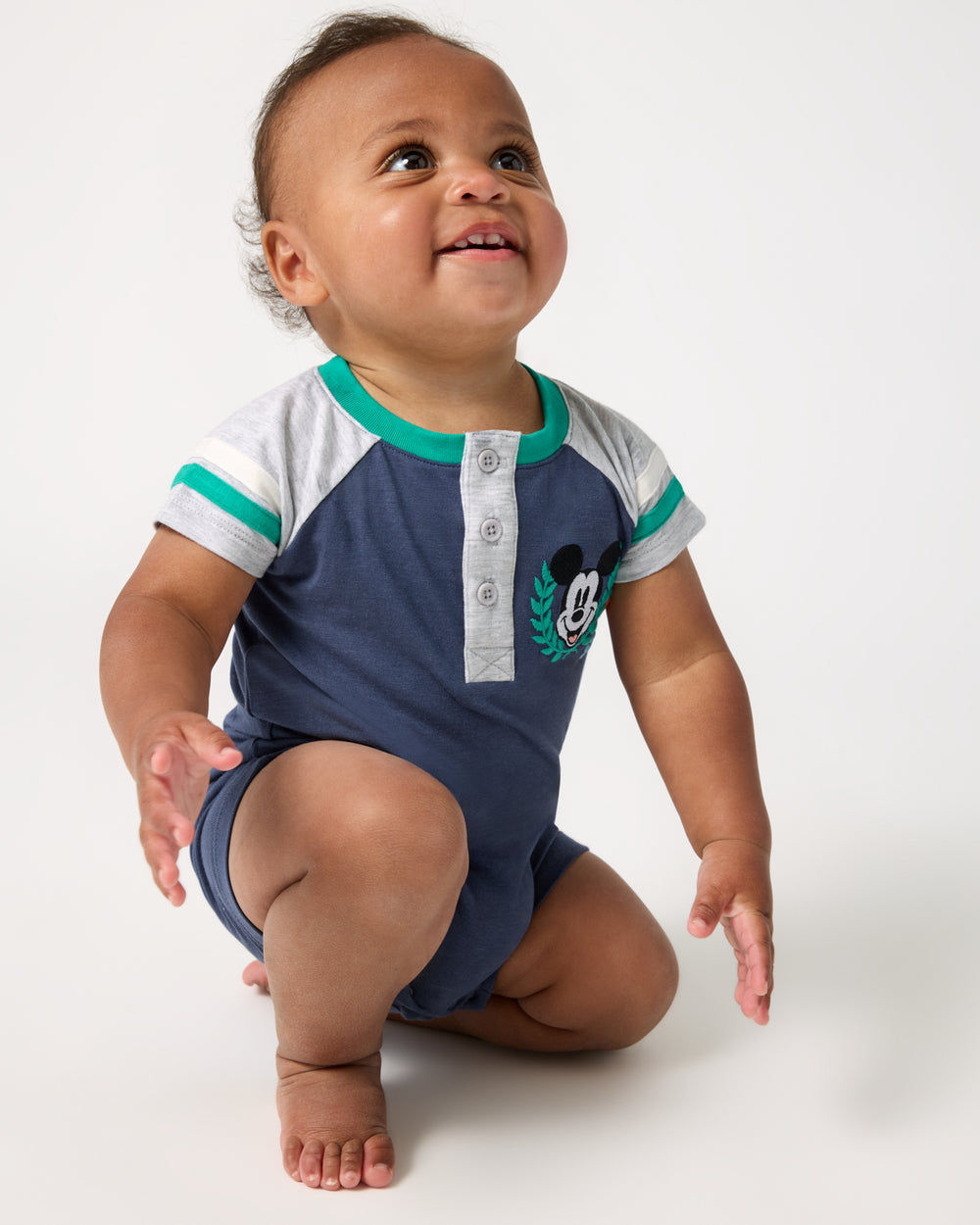 Kneeling baby wearing the Disney Mickey Mouse Sports Club Henley Shorty Romper