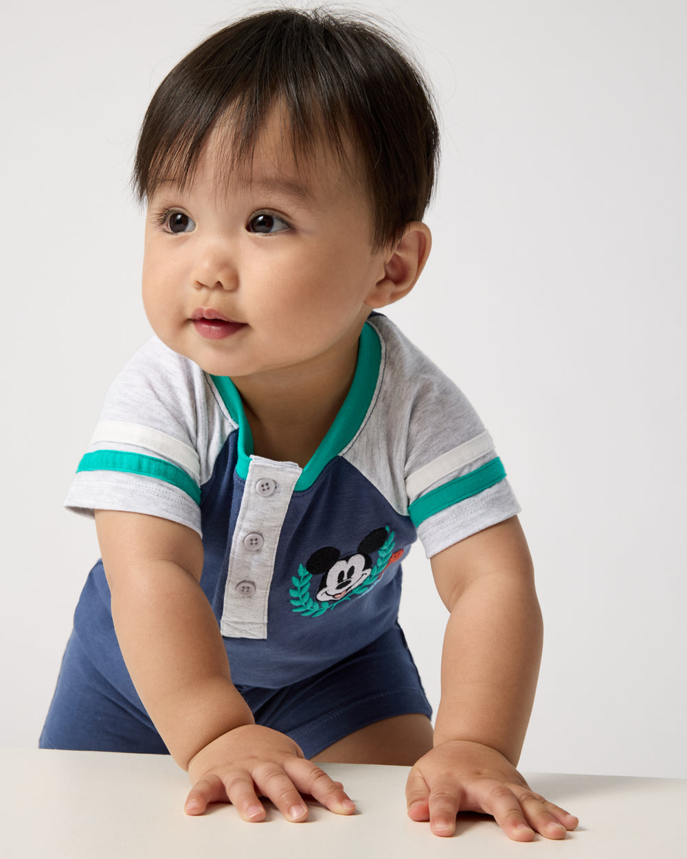 Crawling baby wearing the Disney Mickey Mouse Sports Club Henley Shorty Romper