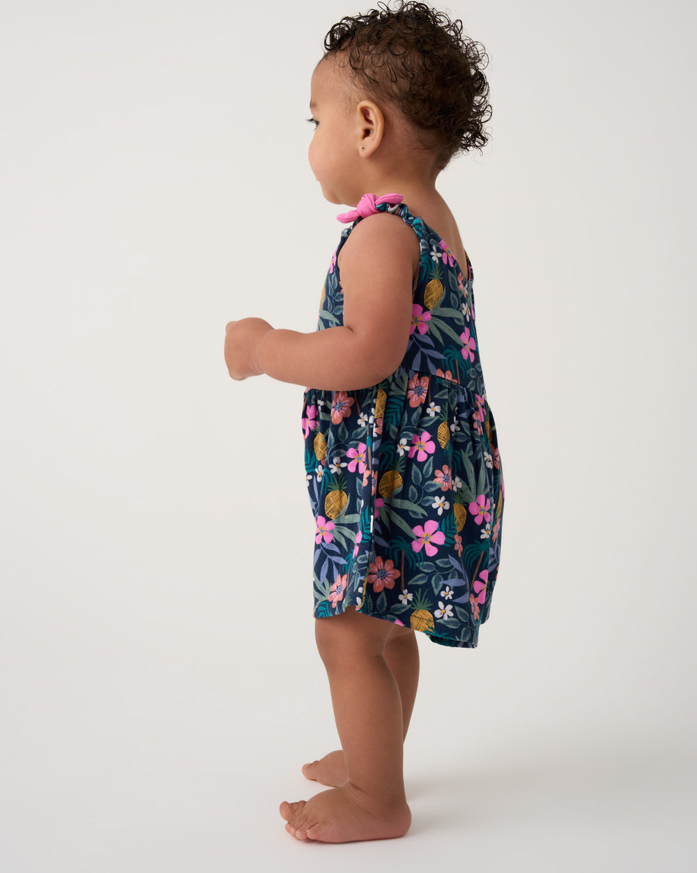 Side view of toddler wearing the Tropical Garden Baby Bow Strap Romper
