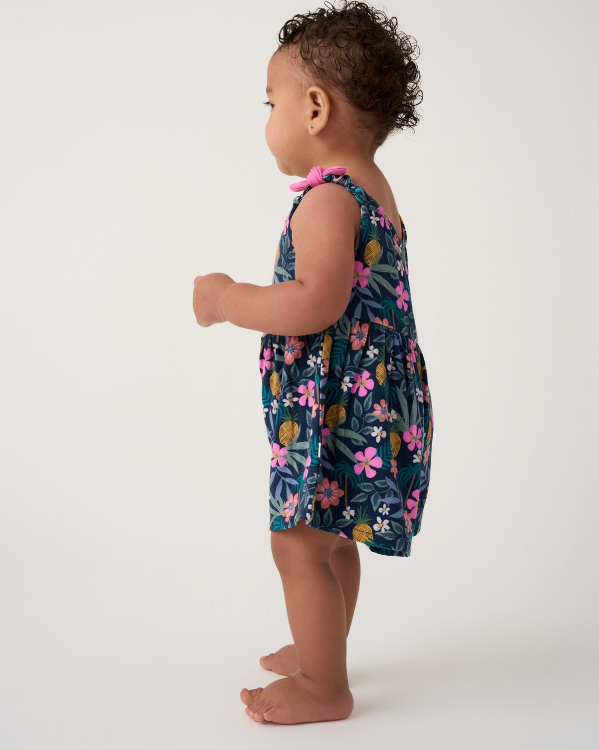 Side view of toddler wearing the Tropical Garden Baby Bow Strap Romper