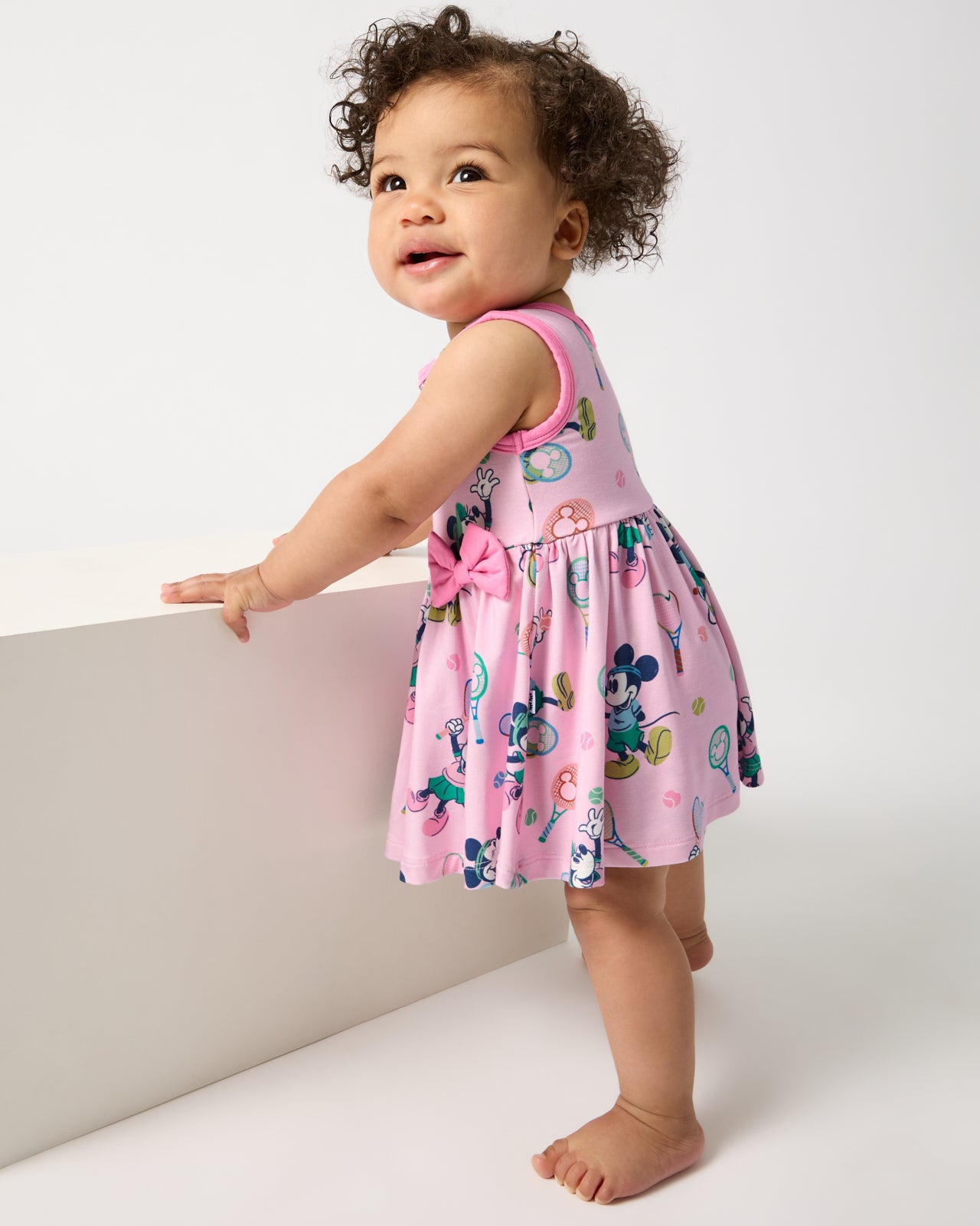 Standing baby wearing the Disney Mickey Mouse & Minnie Mouse Match Twirl Dress with Bodysuit