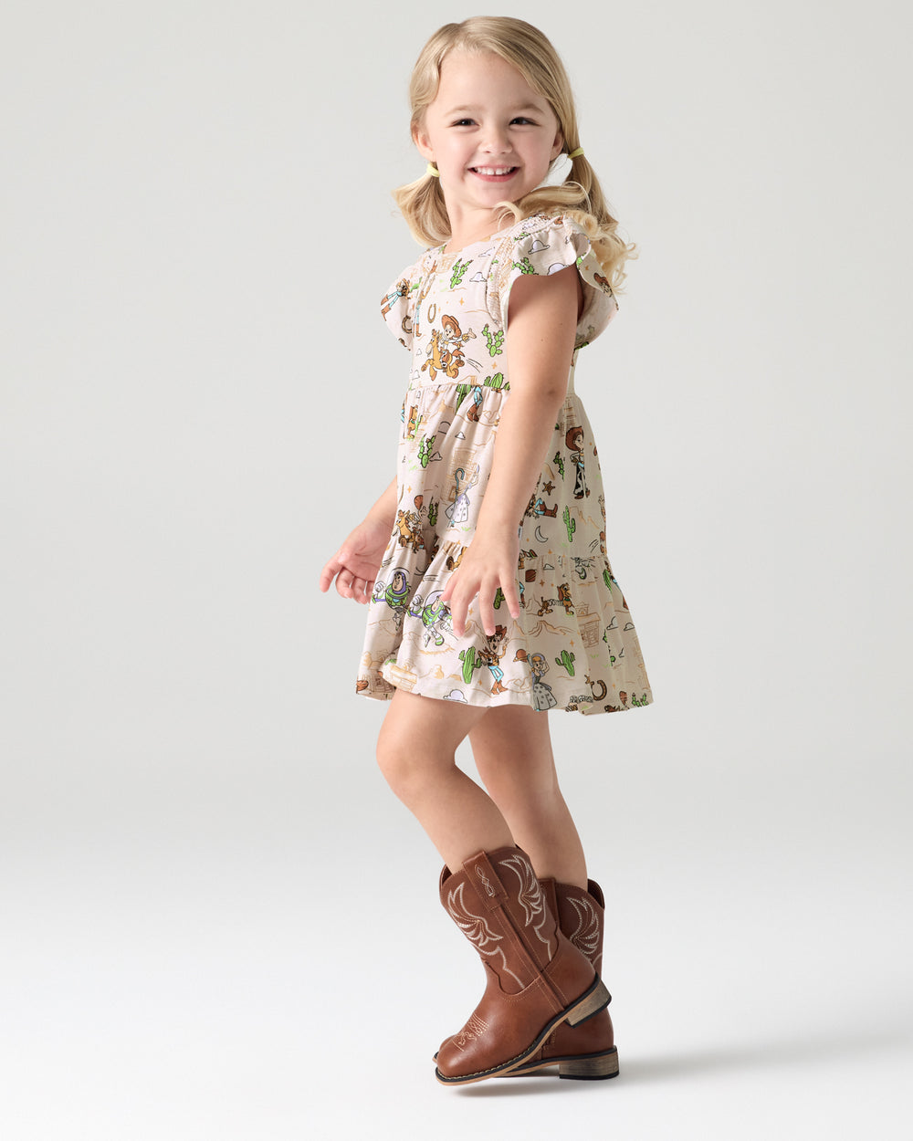Girl wearing the Disney & Pixar Woody's Wild West Tiered Flutter Dress with cowgirl boots
