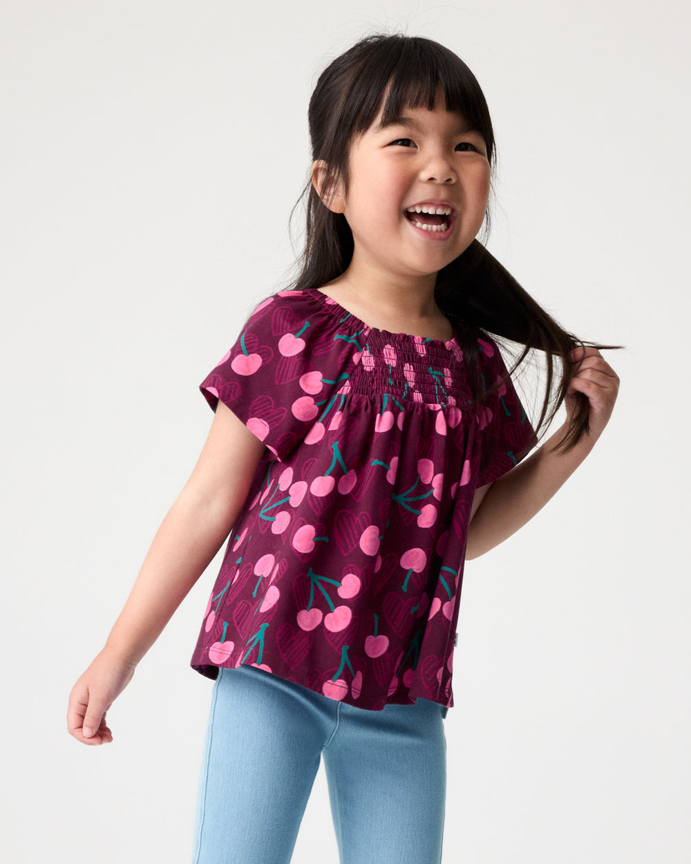 Girl wearing the Cherry Charm Smocked Flutter Top