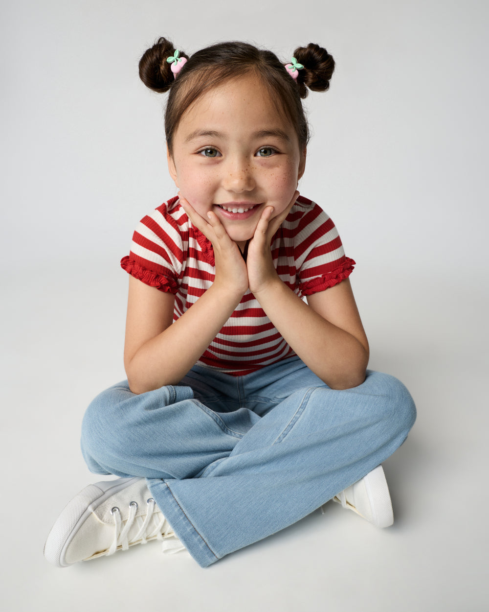 Sitting girl wearing the Red Ember Stripe Ruffle Tee with denim pants