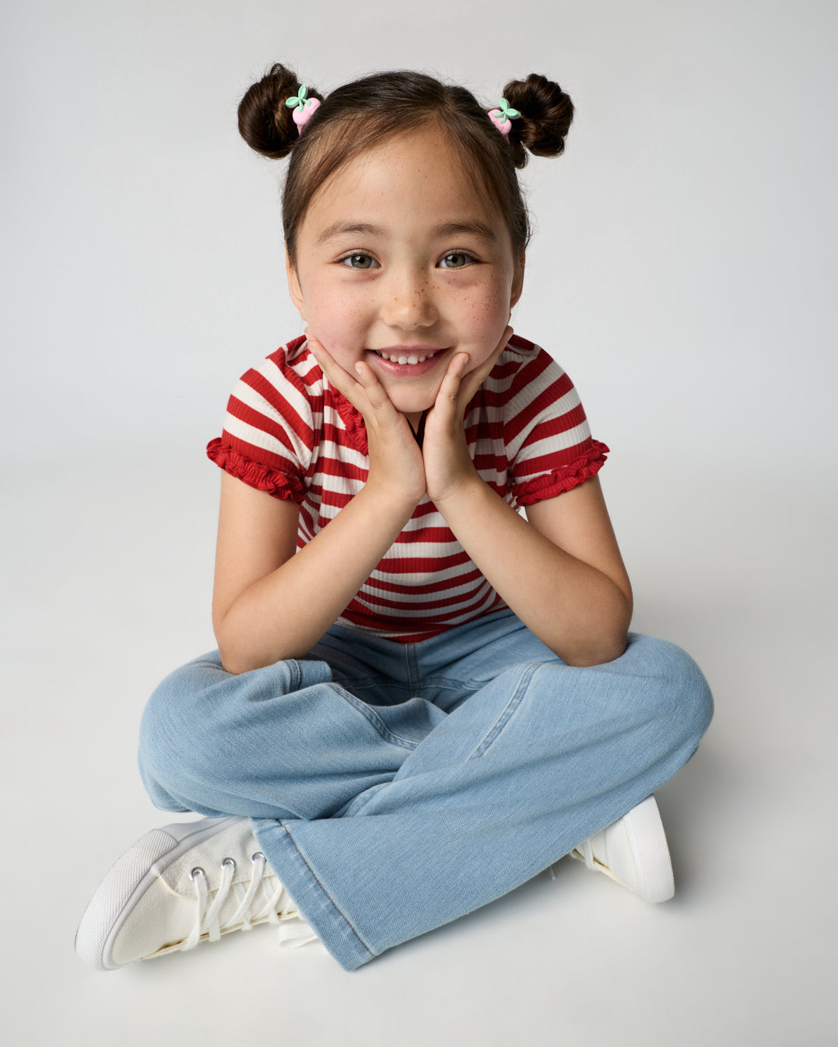 Sitting girl wearing the Red Ember Stripe Ruffle Tee with denim pants