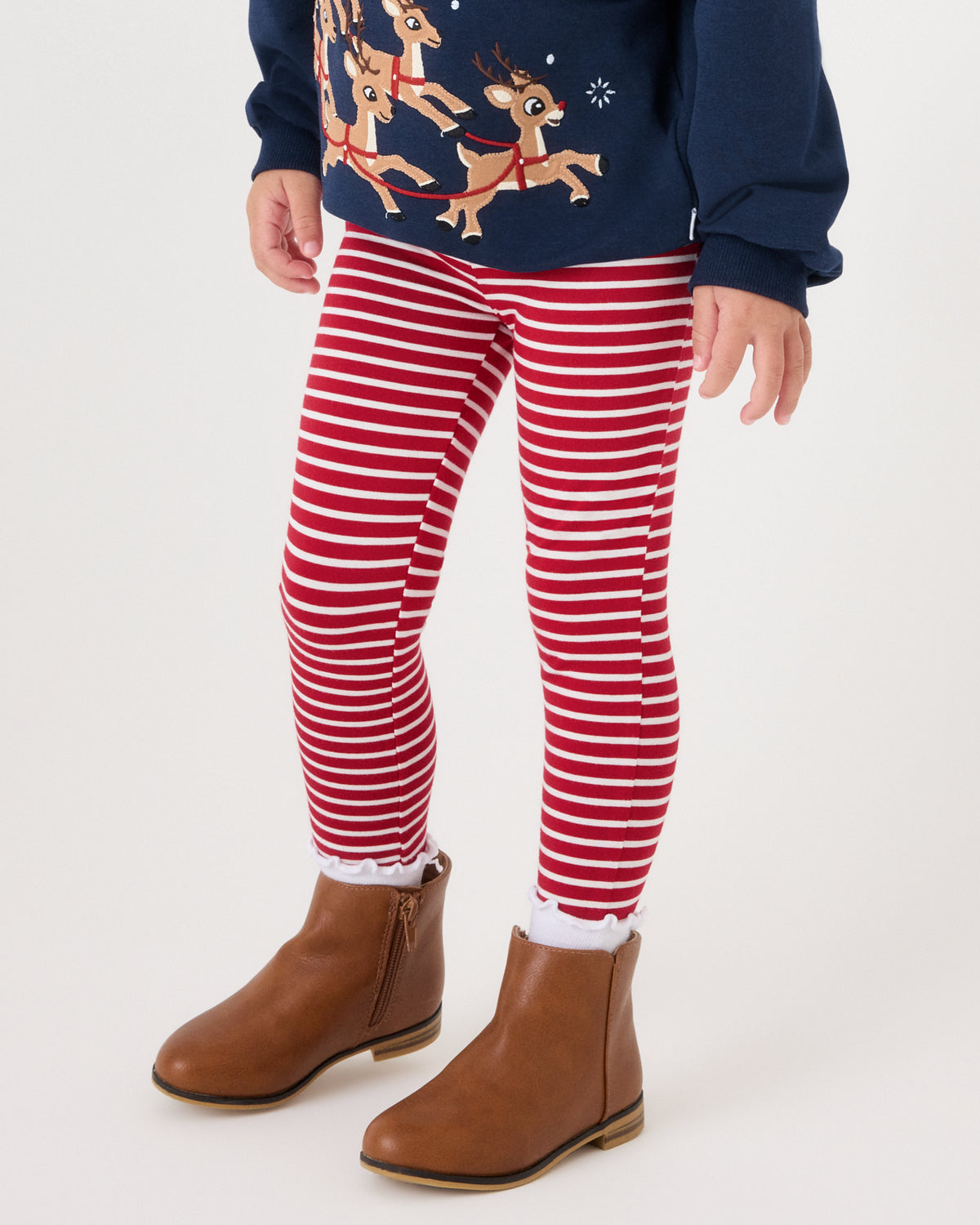 A child wearing red and white striped leggings, a navy blue Christmas sweater with a reindeer graphic, and brown ankle boots, shown from the waist down against a plain light background.
