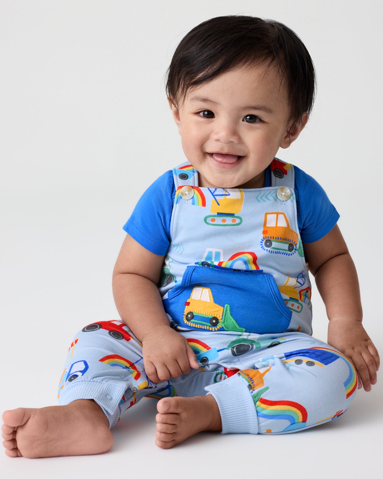 Sitting boy wearing the Rainbow Trucks Overall Set