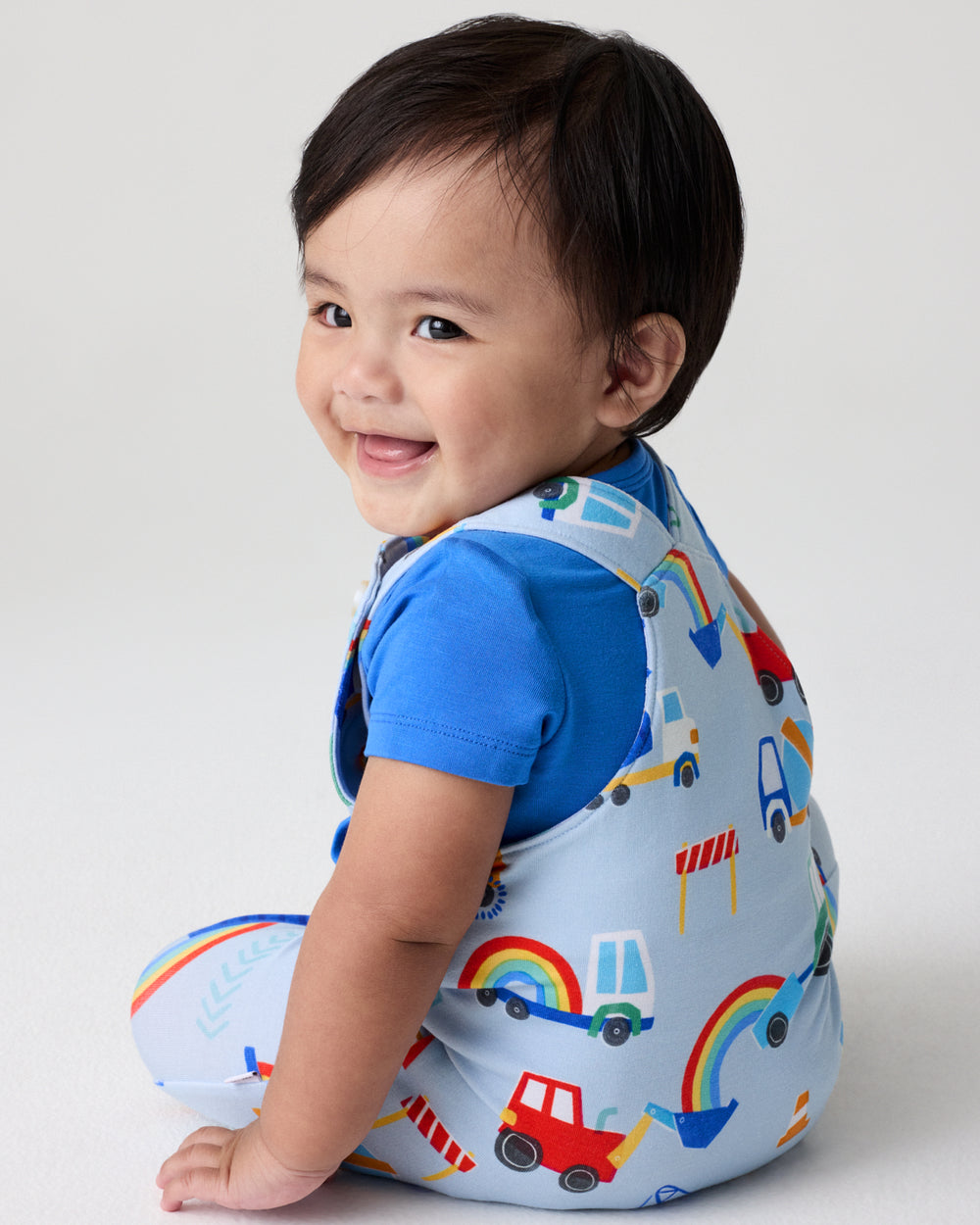 Back view of sitting baby wearing the Rainbow Trucks Overall Set
