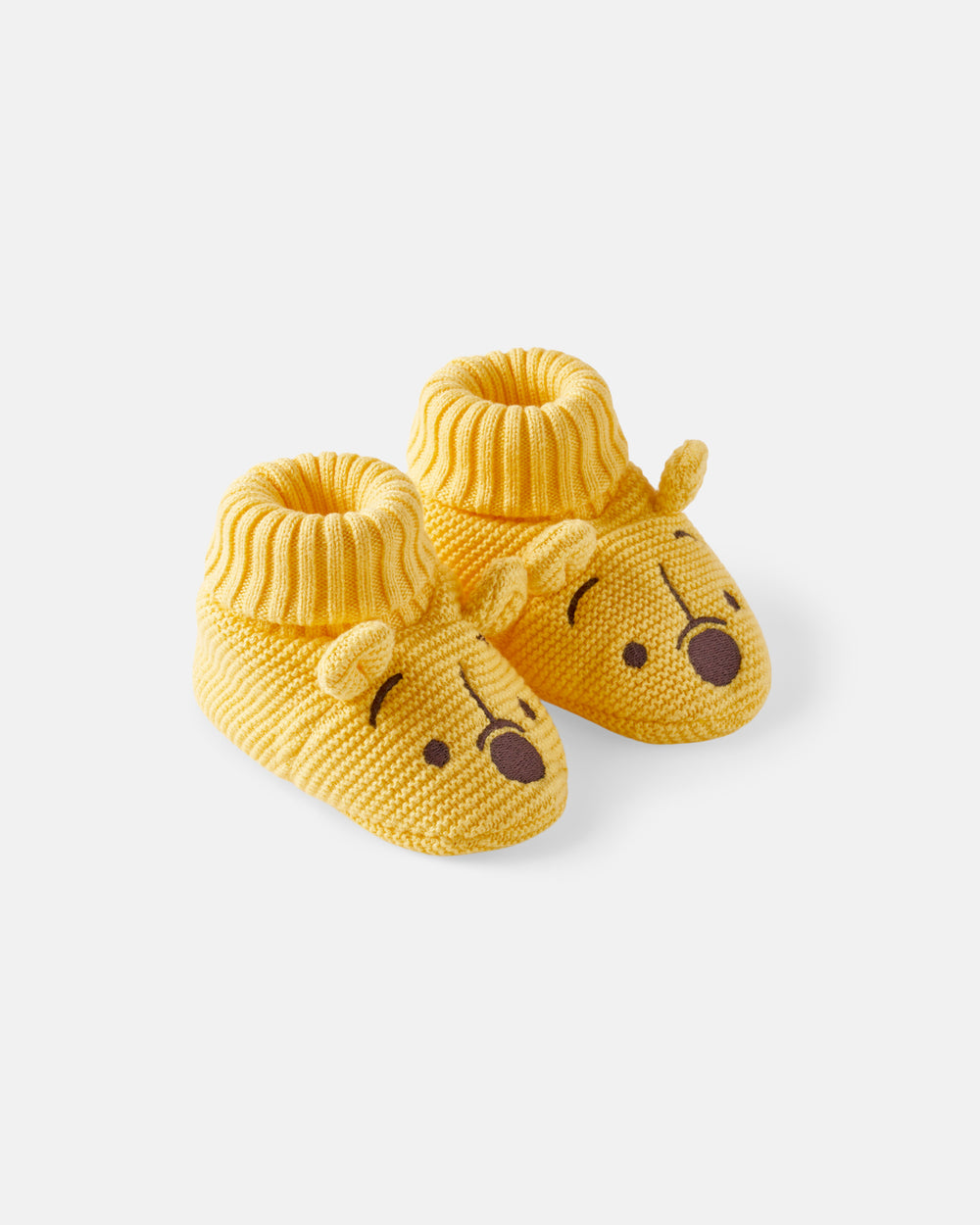 A pair of yellow knit baby booties designed like Winnie the Pooh bear faces, featuring a ribbed cuff and embroidered facial details on a light gray background.