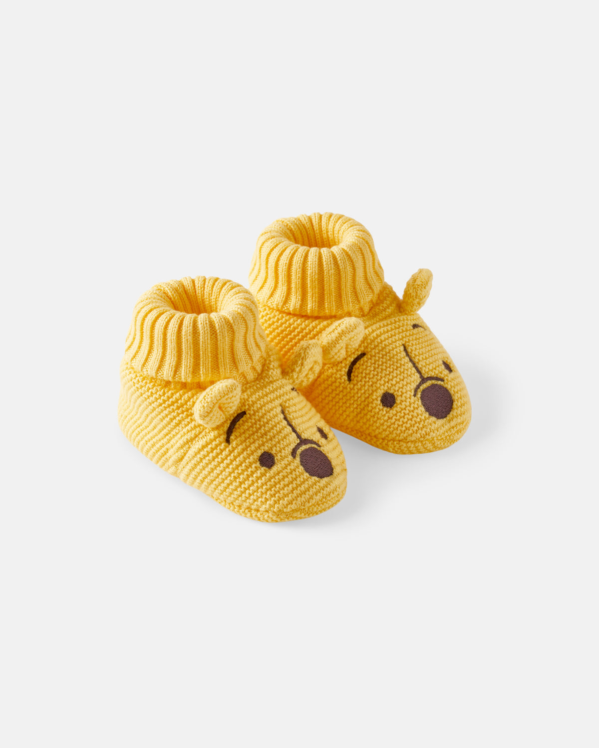 A pair of yellow knit baby booties designed like Winnie the Pooh bear faces, featuring a ribbed cuff and embroidered facial details on a light gray background.