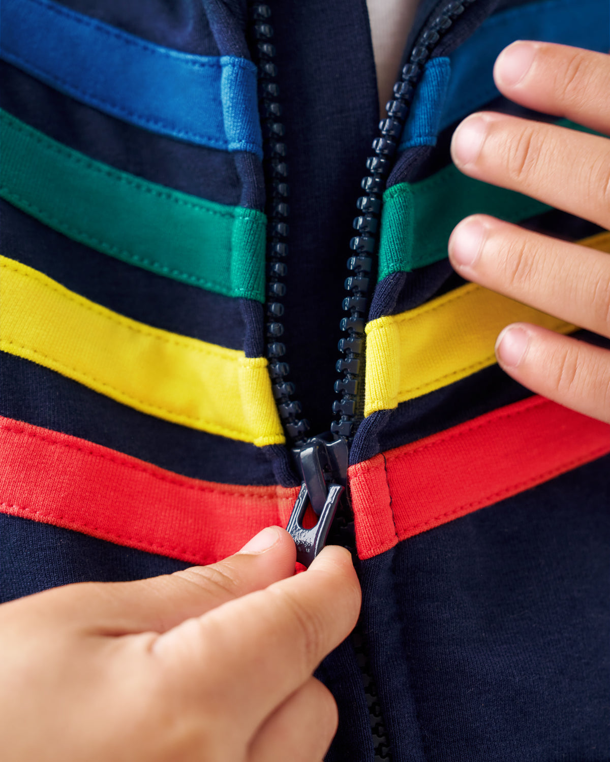 Close-up of a colorful zippered jacket with horizontal stripes in blue, green, yellow, and red, being zipped by hands.