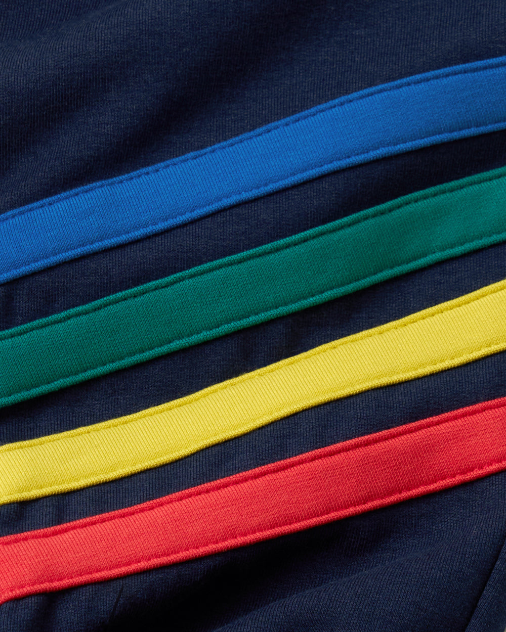 Close-up of a navy blue fabric with four diagonal rainbow stripes in blue, green, yellow, and red.