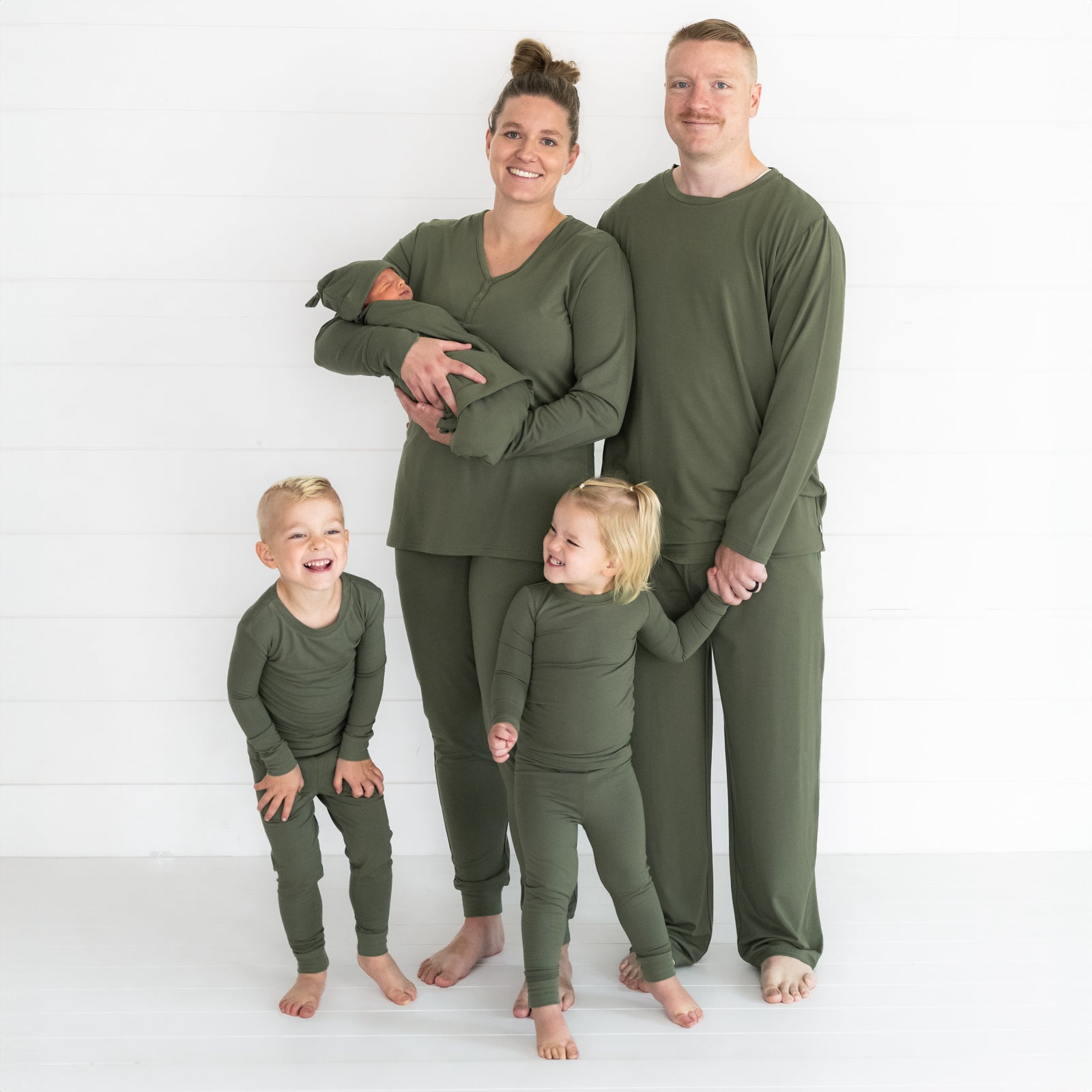 Family of five wearing matching Cozy Olive pjs in men's, women's, and children's swaddle and two piece styles.