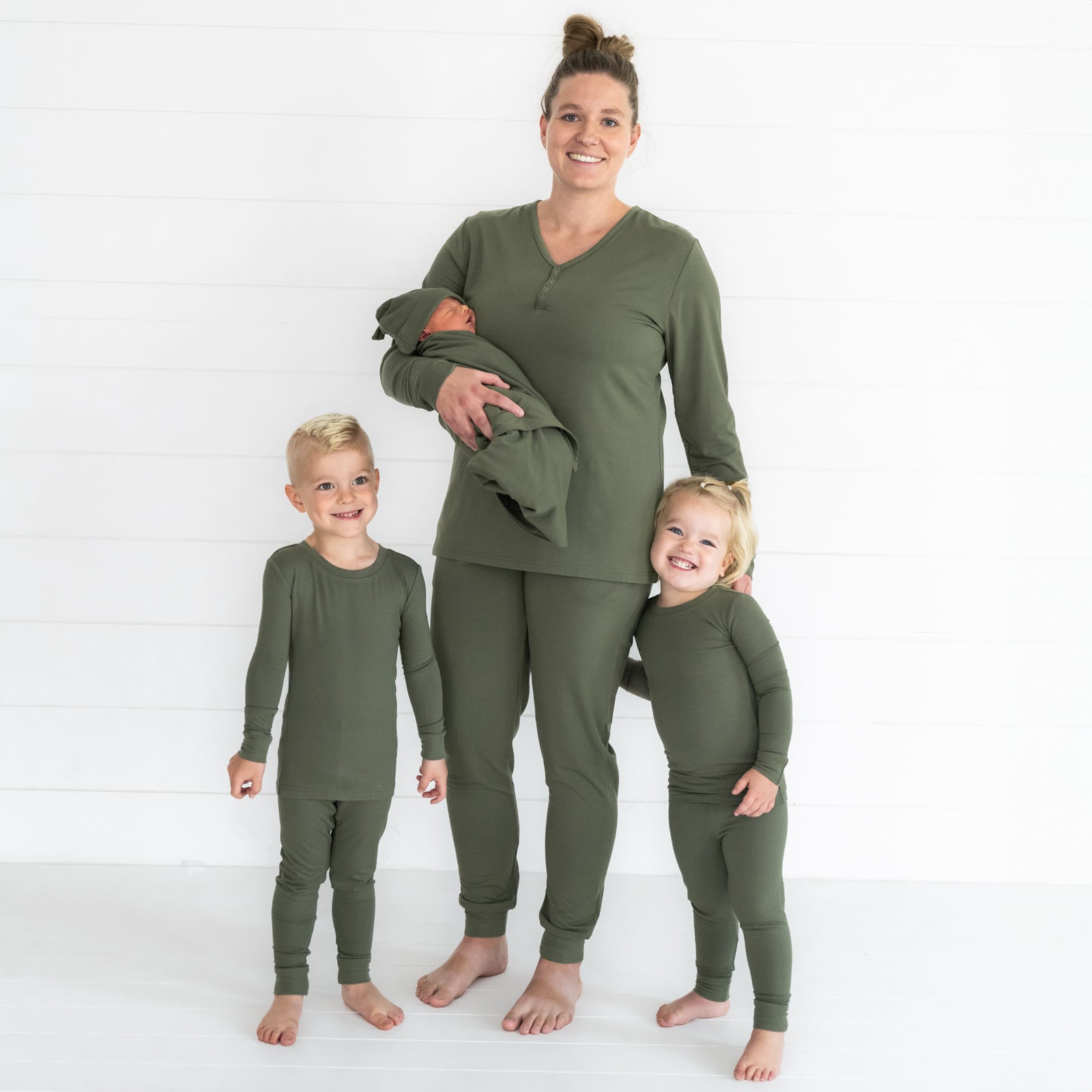 Mother and three children wearing matching Cozy Olive pjs in women's and children's zippy and swaddle styles