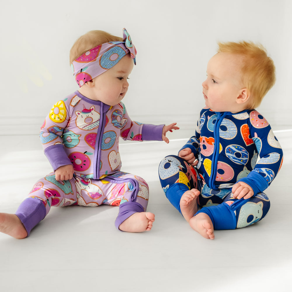 two children sitting together wearing coordinating Lavender and Blue Donut dream zippies. The little girl is pairing her zippy with a matching Lavender Donut Dreams luxe bow headband