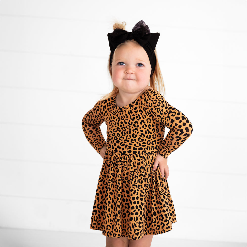 Image of a child with her hands on her hips wearing a Classic Leopard Twirl Dress with Bodysuit and Cat Ears Luxe Bow Headband