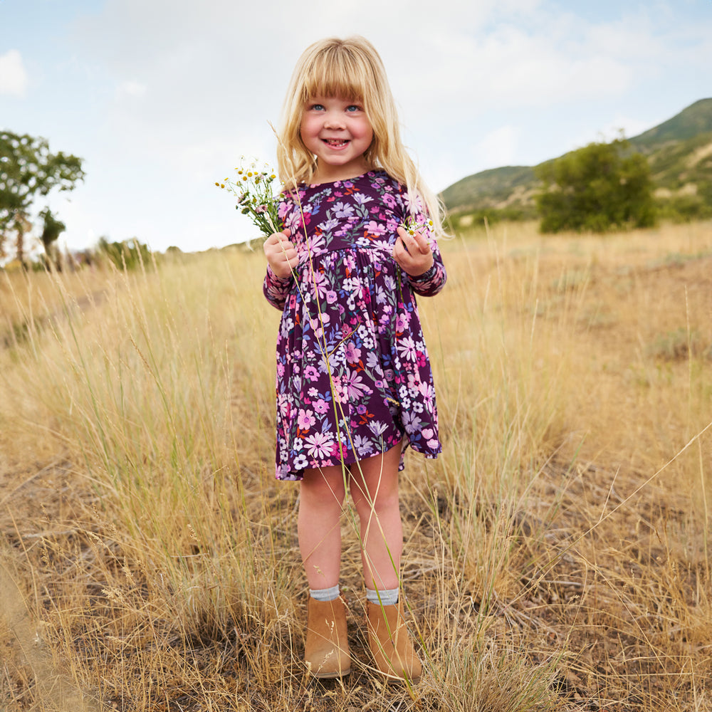 Girl outdoors holding flowers while wearing the Violet Meadow Bow Back Skater Dress