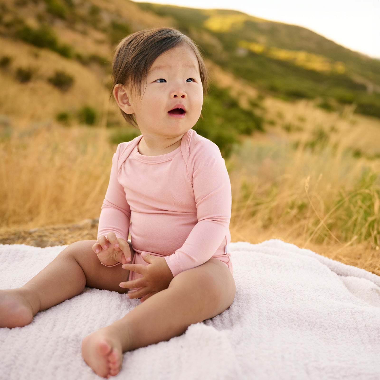 baby sitting on blanket in mauve blush bodysuit.