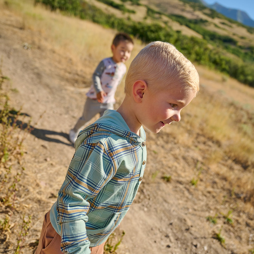 Two boys outdoors walking on a hiking trail. Clear side view image of boy wearing the Forest Plaid Henley Hoodie 