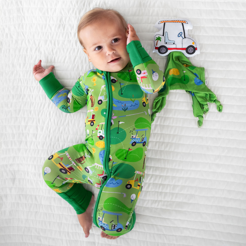 Alternate image of a child laying on a bed wearing a Fairway Fun zippy with Caddie the Golf Cart sleepyhead lovey