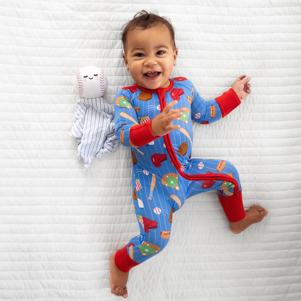 Child laying on a bed wearing Blue All Stars zippy with Major the Baseball sleepyhead lovey
