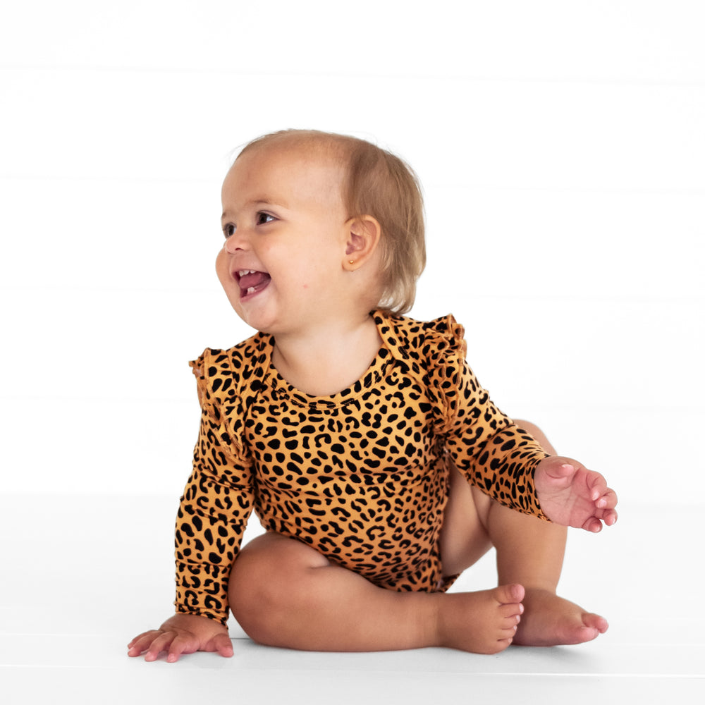 Image of a child sitting on the ground wearing a Classic Leopard Flutter Bodysuit