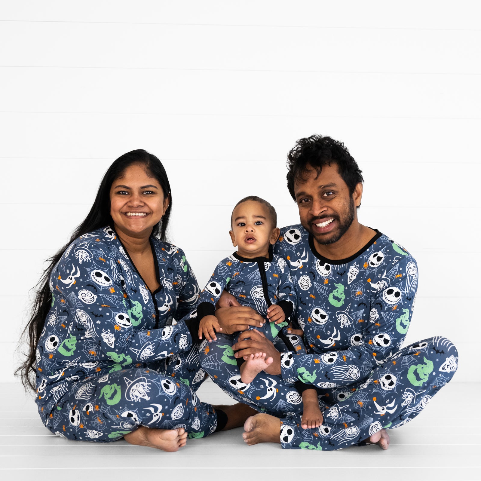 Family of three wearing Disney Jack & Crew printed pajama sets in men's, women's and children's styles. Child is wearing a zippy style.