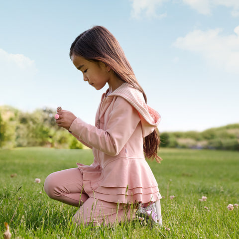 Girl kneeling in the grass wearing a mauve blush peplum hoodie