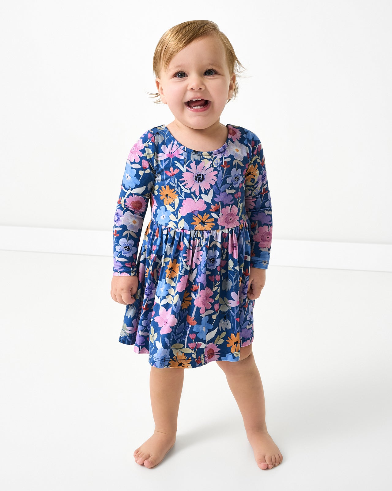 Standing baby wearing the Dusk Blooms Bow Back Skater Dress with Bodysuit