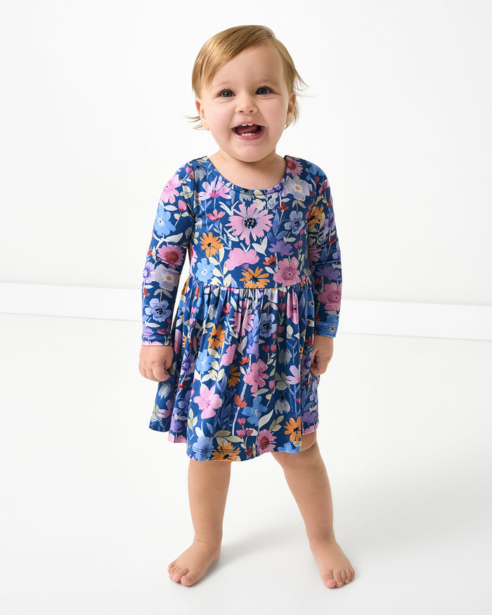 Standing baby wearing the Dusk Blooms Bow Back Skater Dress with Bodysuit