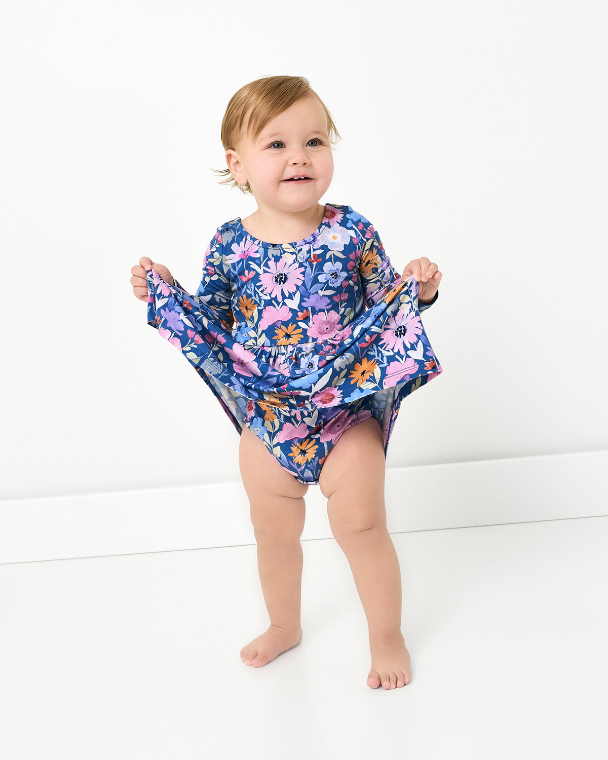 Baby wearing the Dusk Blooms Bow Back Skater Dress with Bodysuit holding up the skirt