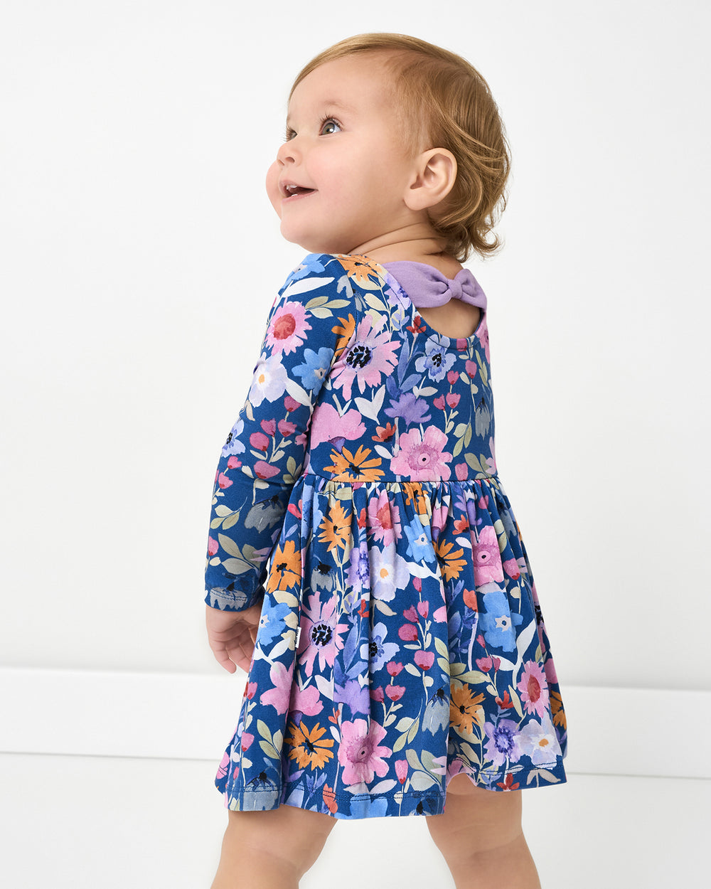 Back view of baby wearing the Dusk Blooms Bow Back Skater Dress with Bodysuit