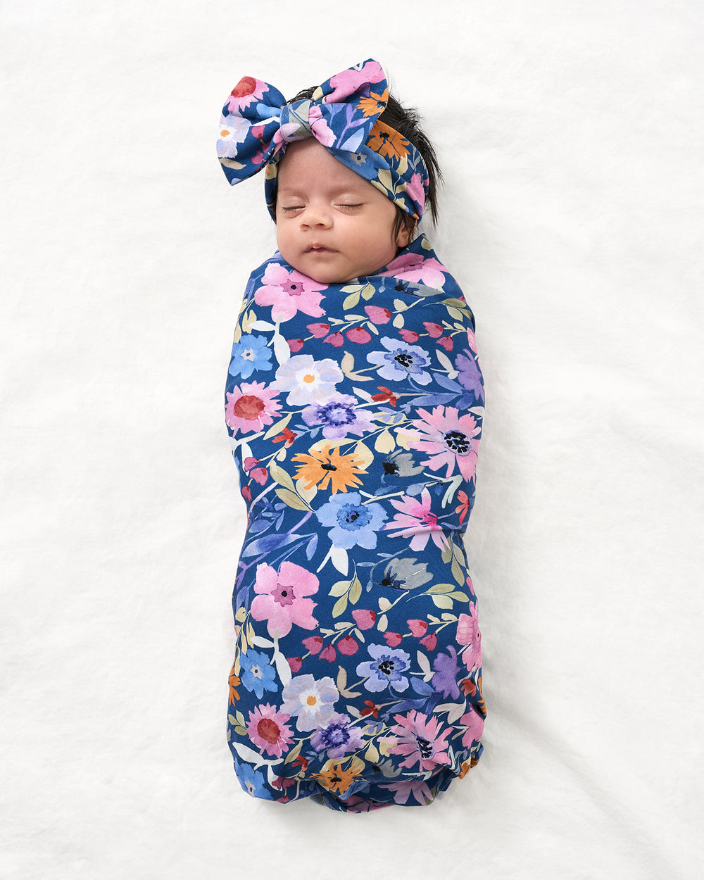 Aerial view of baby wearing the Dusk Blooms Swaddle & Luxe Bow Headband Set