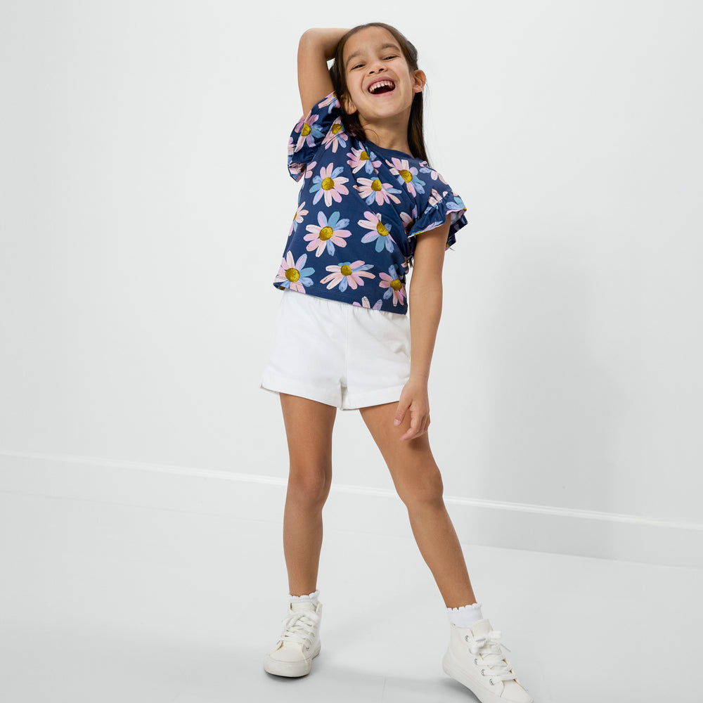 Standing child wearing the Daisy Blooms Flutter Tee with the bright white denim shorts