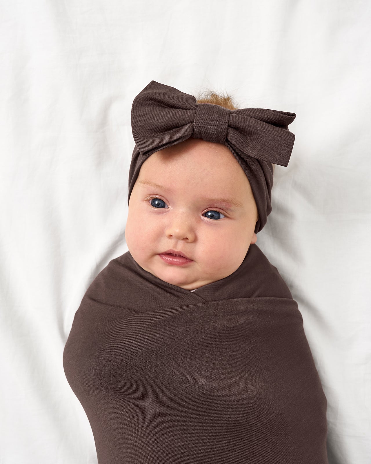 Close up of baby wearing the Dark Chocolate Swaddle & Luxe Bow Headband Set