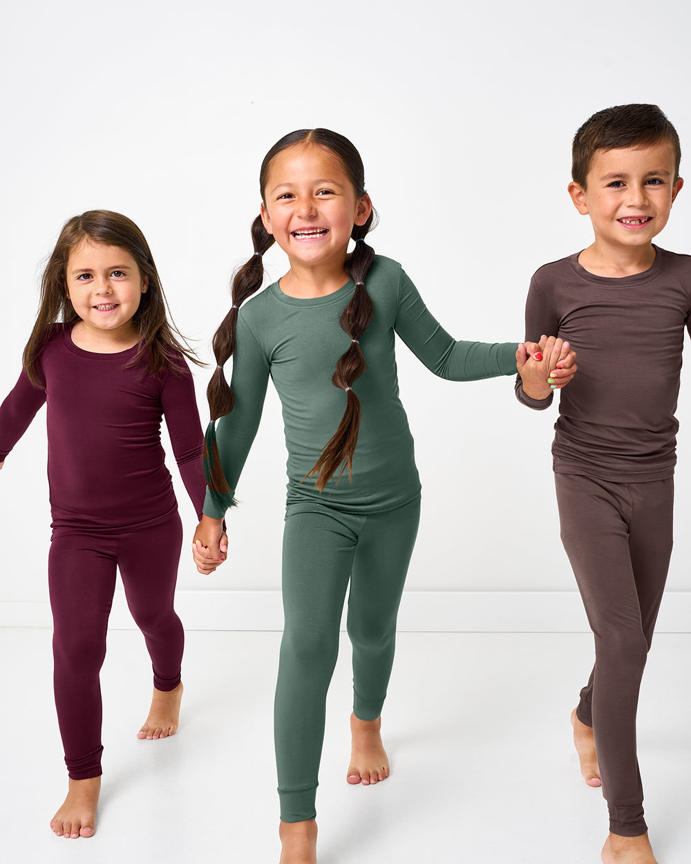 Three children in motion wearing pajama sets from the Fall Solids collection
