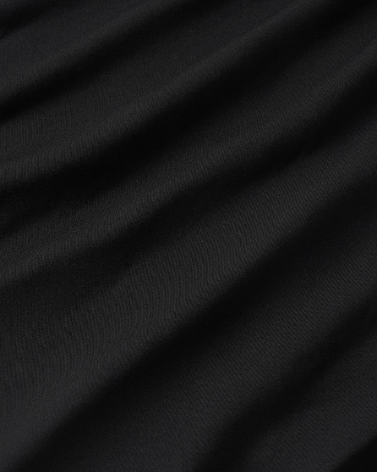 A close-up of draped black fabric with soft diagonal folds and a smooth matte texture.