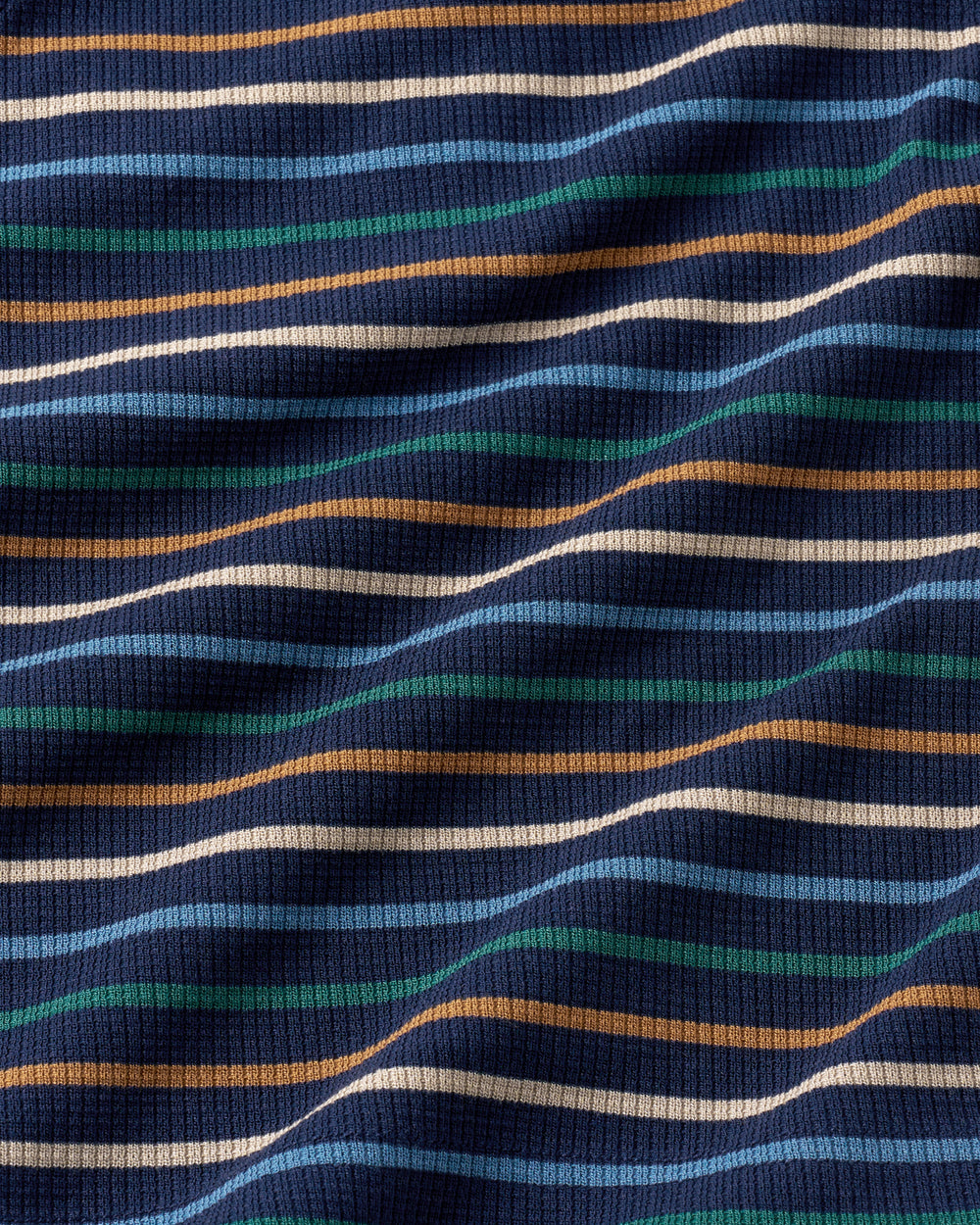A close-up of a ribbed waffle fabric with horizontal wavy stripes in navy blue, light blue, teal green, tan, and cream.